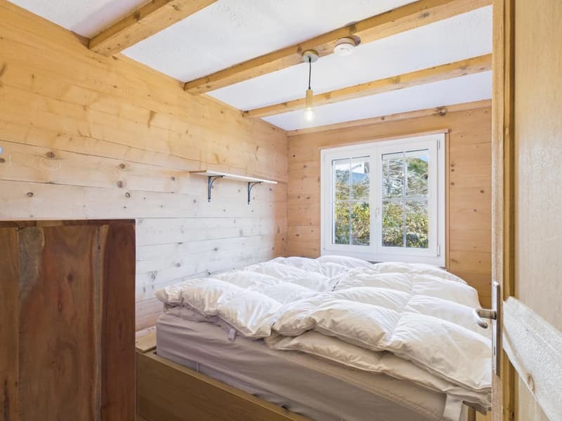 wooden bed with white pillows, white walls, small window