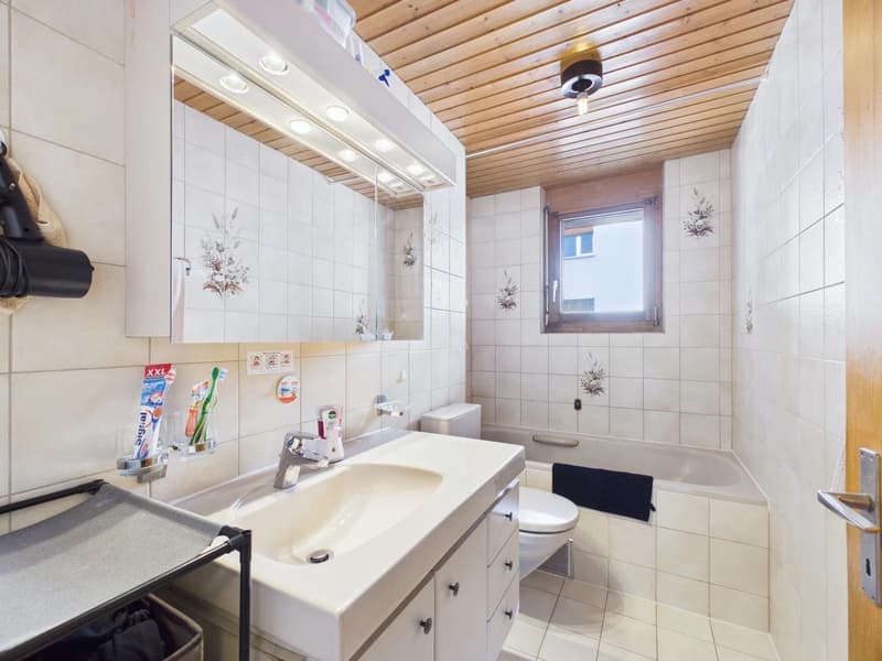 white tiles, modern bathroom fixtures, bathtub, white toilet, wooden ceiling, large mirror, small window
