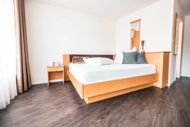A bedroom with a wooden bed, white sheets, pillows, a nightstand, a mirror, and a lamp