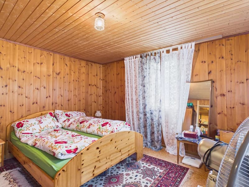 wooden bed, floral bedspread, wooden nightstand, lamp, rug, wooden wall, curtain, mirror, fan
