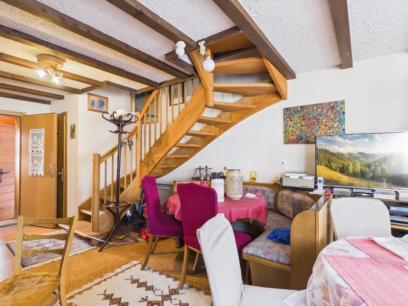 Dining area with wooden staircase, dining table, chairs, TV, rug, and decorative items