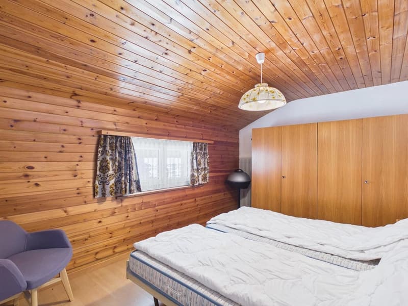 bedroom with wooden walls, two single beds, wooden chair, wooden wardrobe, window with curtains, lamp