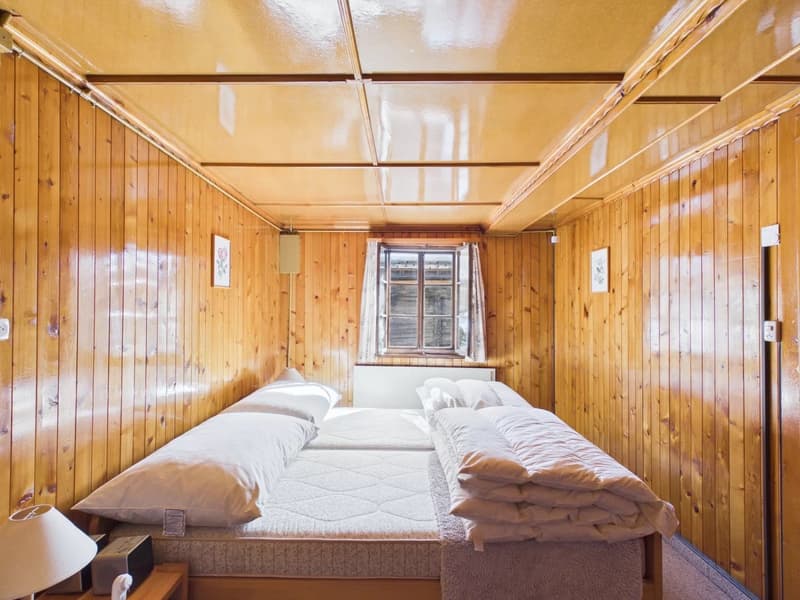wooden walls, white bedding, small window, lamp, speaker