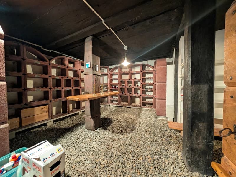 Wine cellar with wooden shelves, wooden table, candles, gravel floor, wooden beams, wooden door