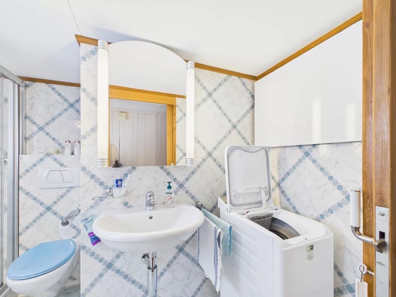 white sink, blue toilet, shower, washing machine, mirror, blue and white tiles