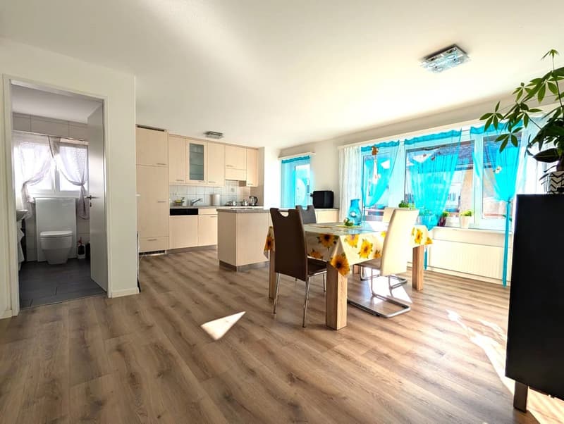 Dining room with wooden floor, dining table, chairs, kitchen with cabinets, sink, stove, refrigerator, and a toilet room with toilet