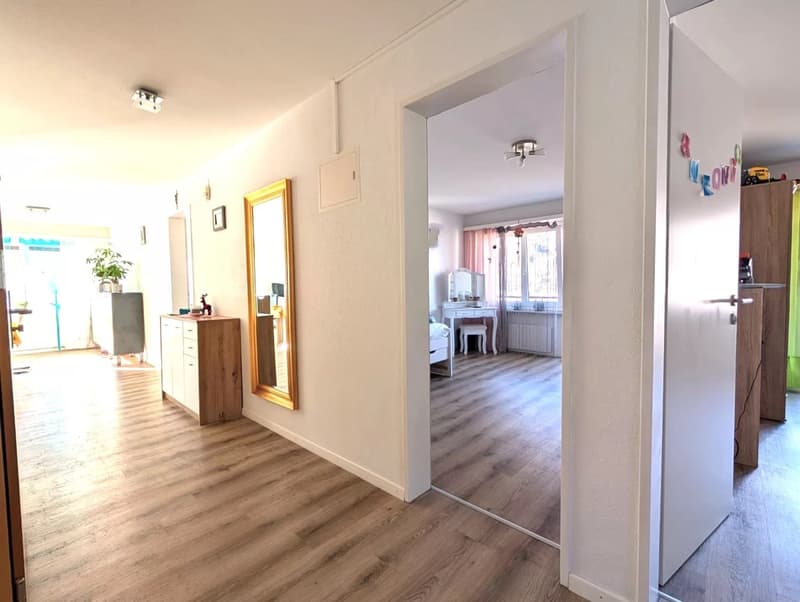Empty room with wooden floor, white walls, wooden cabinet, mirror, and a window with curtains