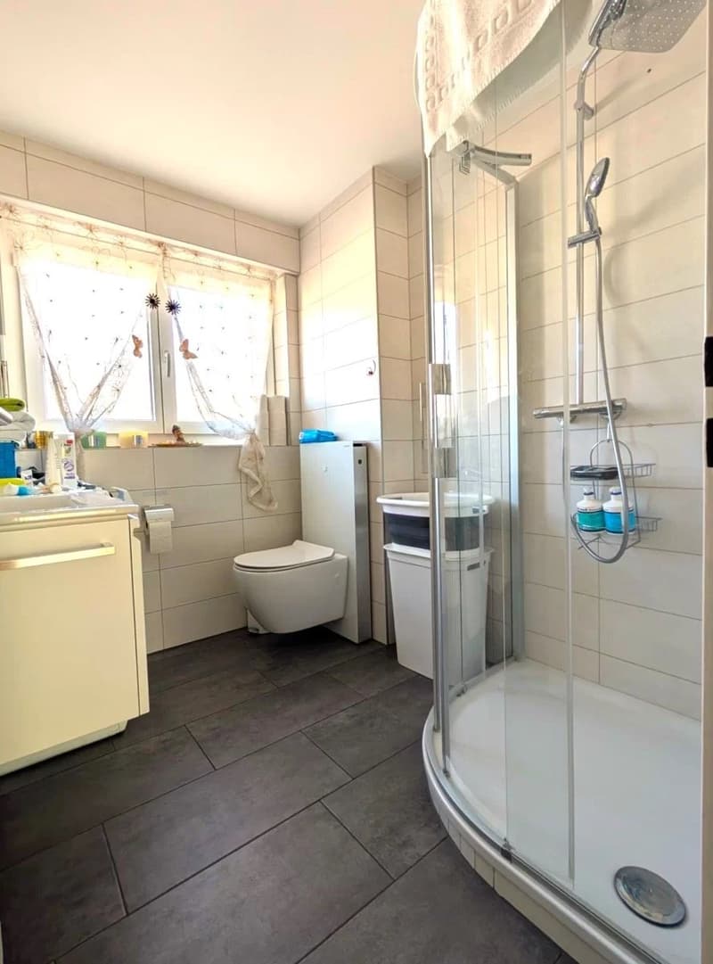 modern bathroom with white tiles, glass shower, white toilet, white sink, white cabinet, window with curtains