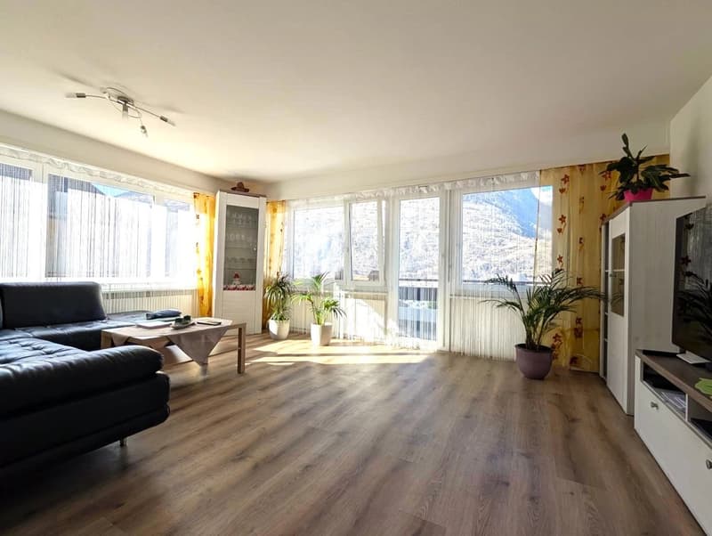 modern living room with wooden floor, large windows, couch, coffee table, plants, TV, cabinets, and a view of the mountains