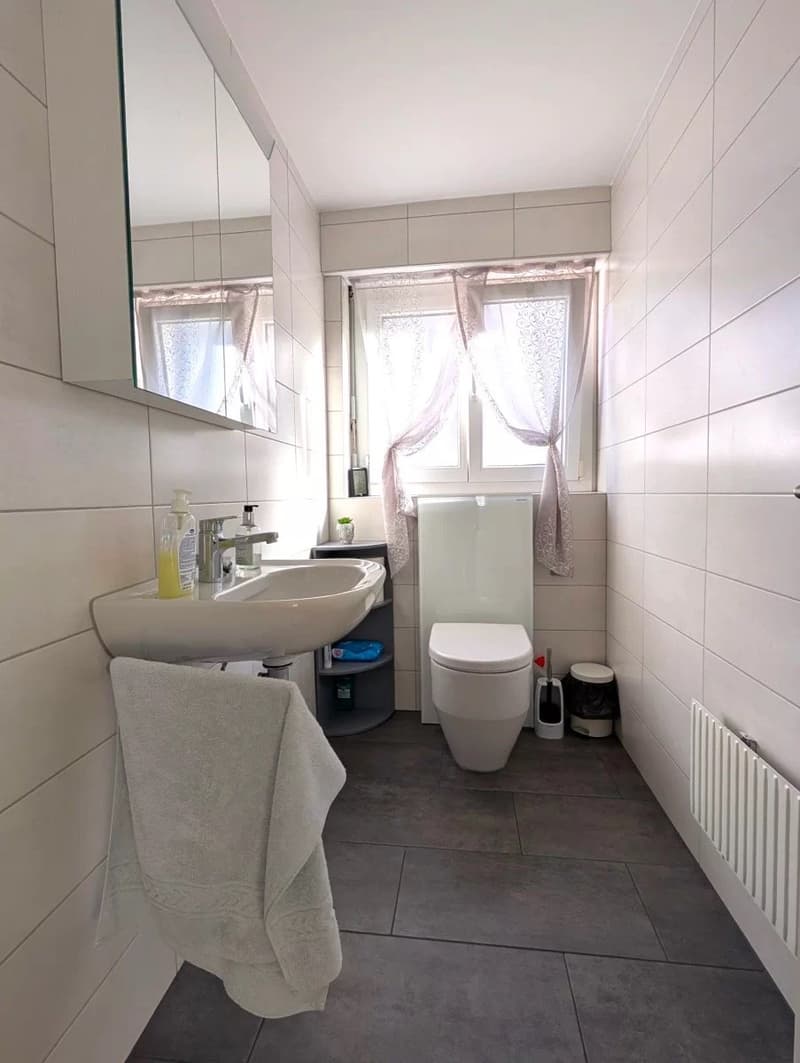 modern bathroom with white tiles, white sink, white toilet, white towel, white mirror, white radiator