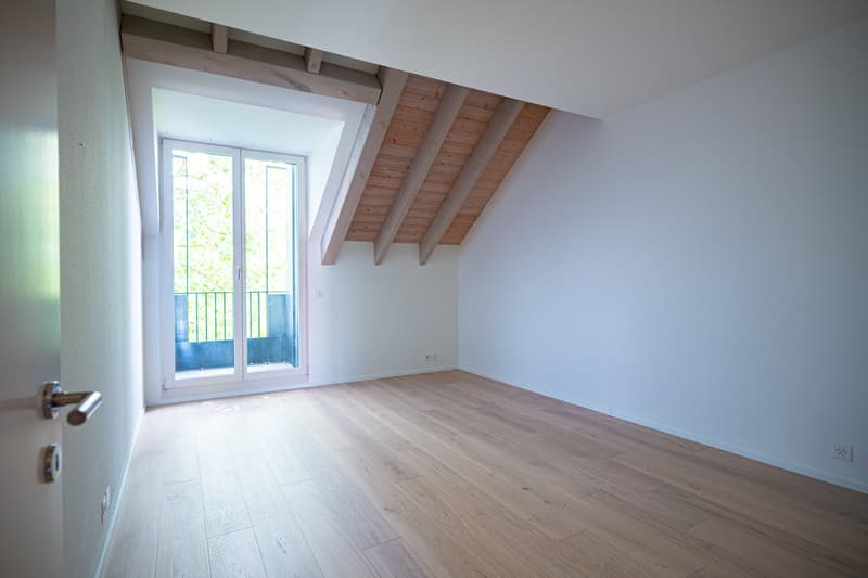 Spacious bedroom with wooden beamed ceiling, large window with balcony access, and hardwood flooring.