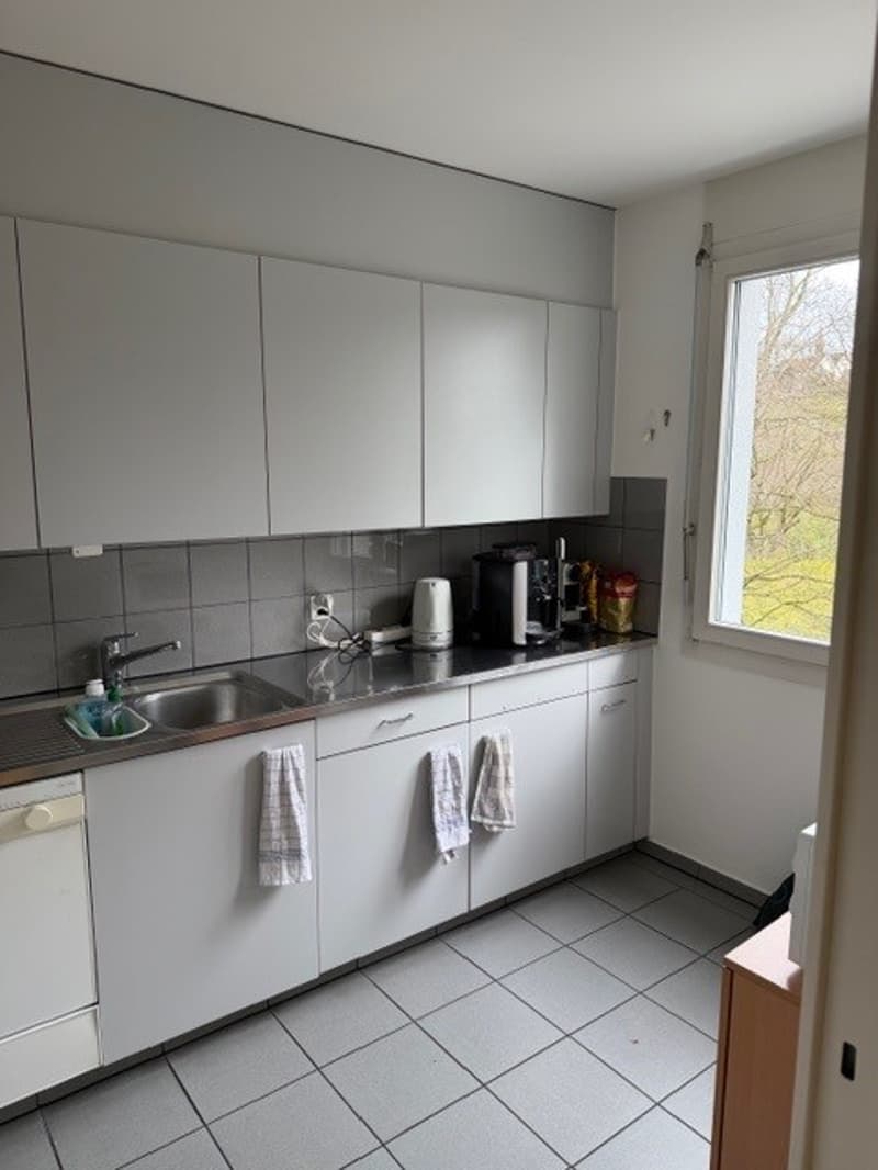 modern kitchen with white cupboards, tiled floor, a window, a sink, a faucet, a coffee machine, a white pitcher, a power outlet, and a tiled wall