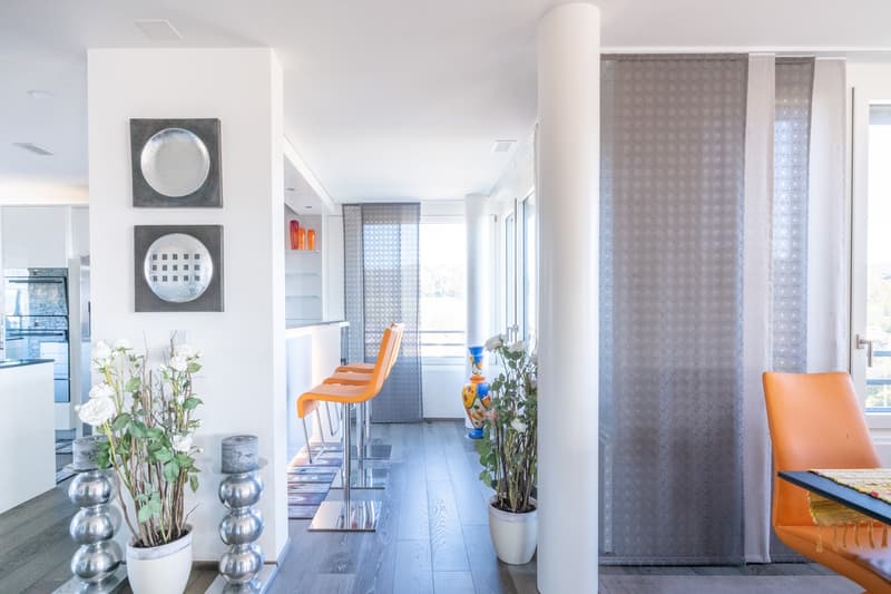 Open kitchen with island, dining area with chairs, floor and wall tiles, windows with curtains, artwork