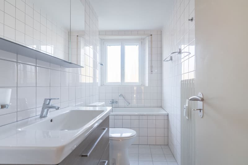 modern bathroom with white tiles, bathtub, toilet, sink, mirror, and cabinet