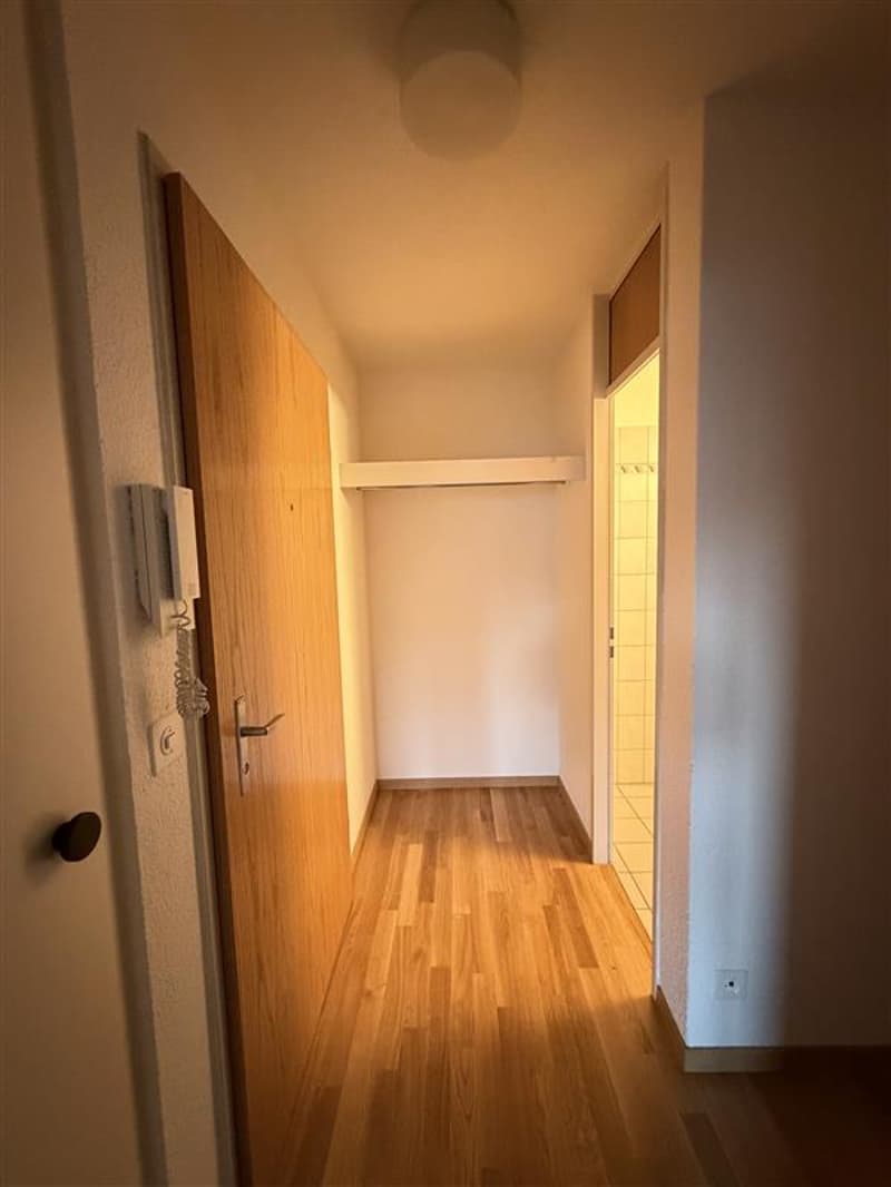 Empty hallway with wooden floor, white walls, open door, and a telephone on the wall