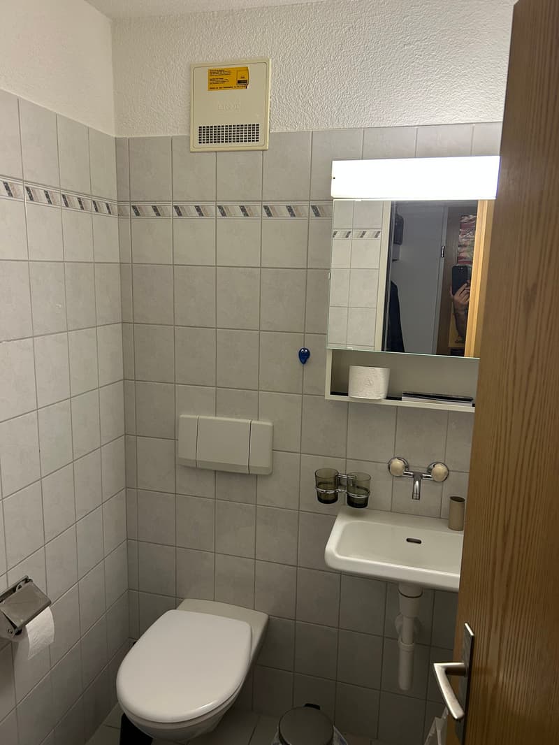 small bathroom with toilet, sink, mirror, and air conditioning unit