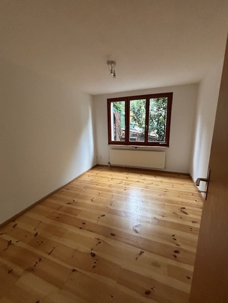 Empty room with wooden floor, white walls, radiator and window