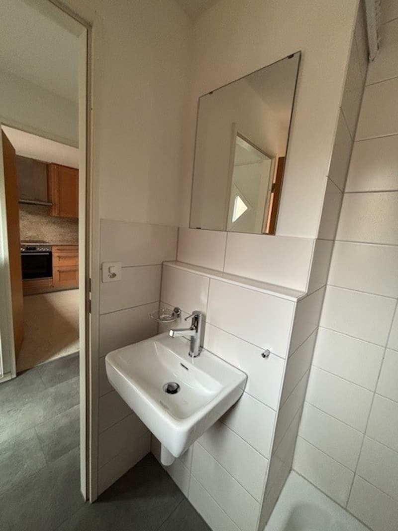 Modern white tiled bathroom with a vanity, sink, faucet, mirror, and bathtub.