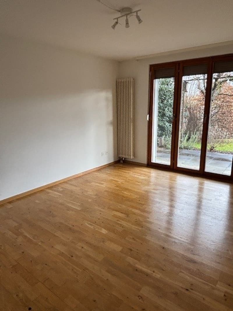 Large open room with wooden floor, glass door, radiator, and balcony