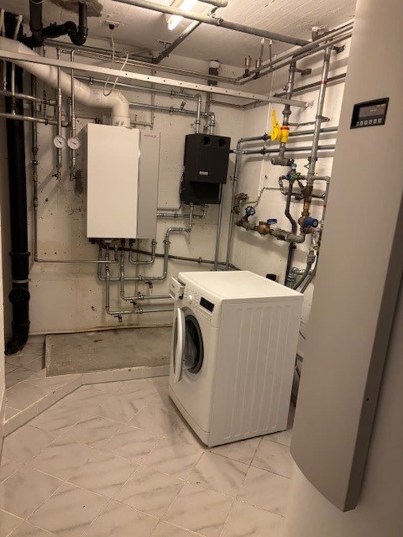 A small utility room with washing machine and pipes