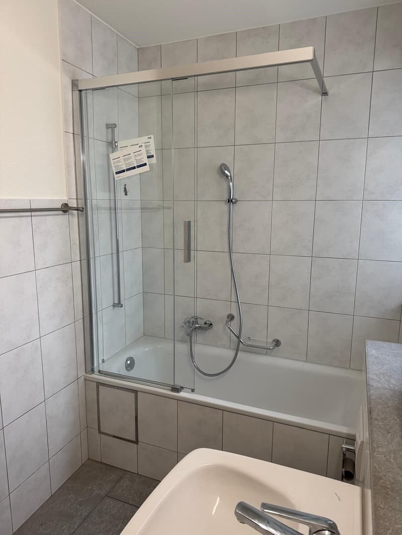 Bathroom with a bathtub, shower, sink, and tiled walls and floor.