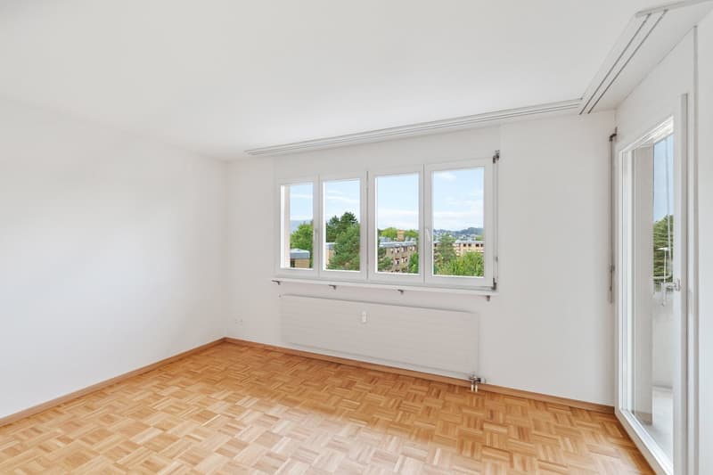 Empty room with white walls, parquet flooring, large window with city view, sliding glass door