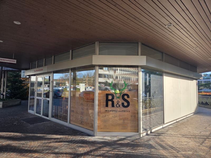 Facade of a building, large glass windows, entrance door, name 'R&S', wooden decoration, brick floor