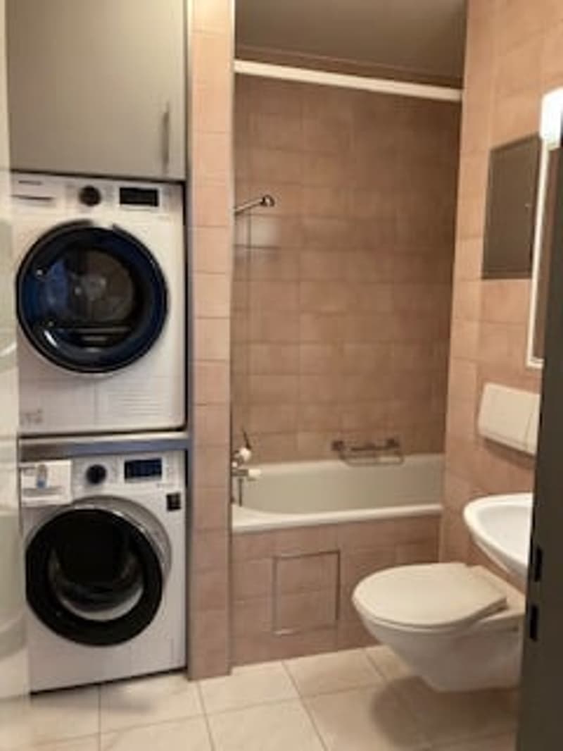 Small bathroom with a stacked washer and dryer, a bathtub, a toilet, and a sink.