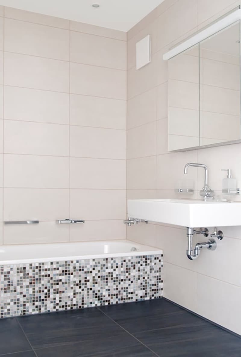 Modern bathroom with white tiles, blue tile border around bathtub, a free-standing bathtub, a white sink, and a mirror.