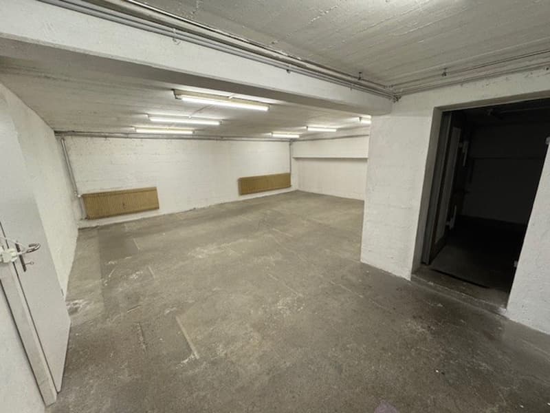 empty underground parking area, concrete floor, two heaters on the wall, ceiling lights, doors on the left and right