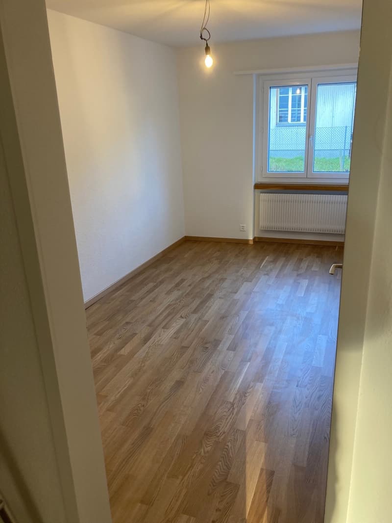 large empty room with wooden floors, white walls, single window