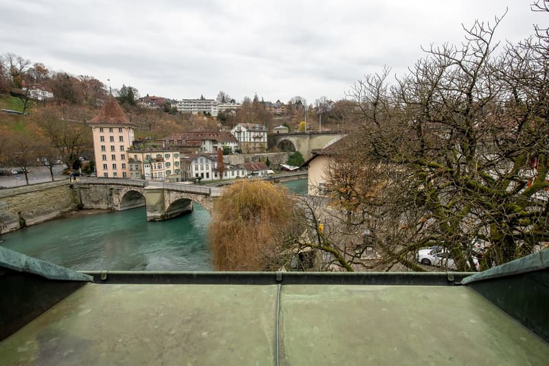 Aerial view of a building with a bridge over a river, surrounded by trees and buildings