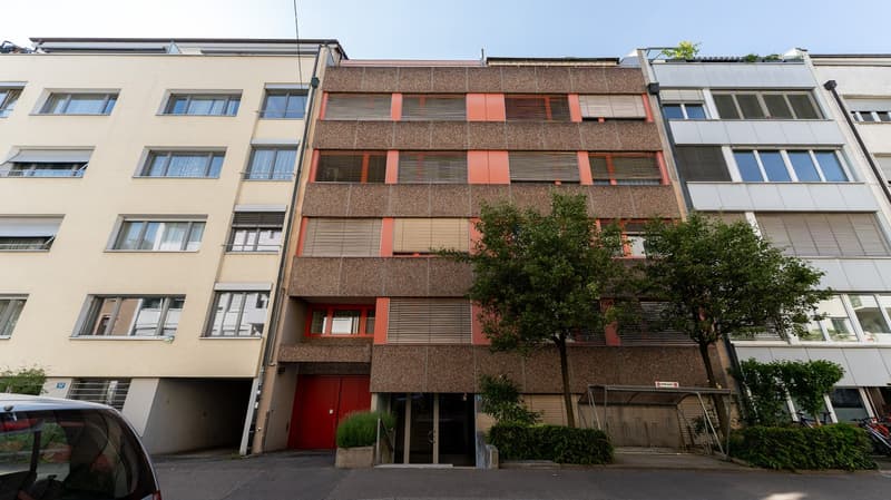 Modern multistory apartment building with multiple balconies, garage entrance, trees, and bicycle racks