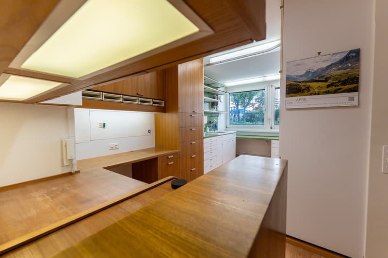 wooden cabinets, open layout, wooden countertops, white sink, window, calendar on wall