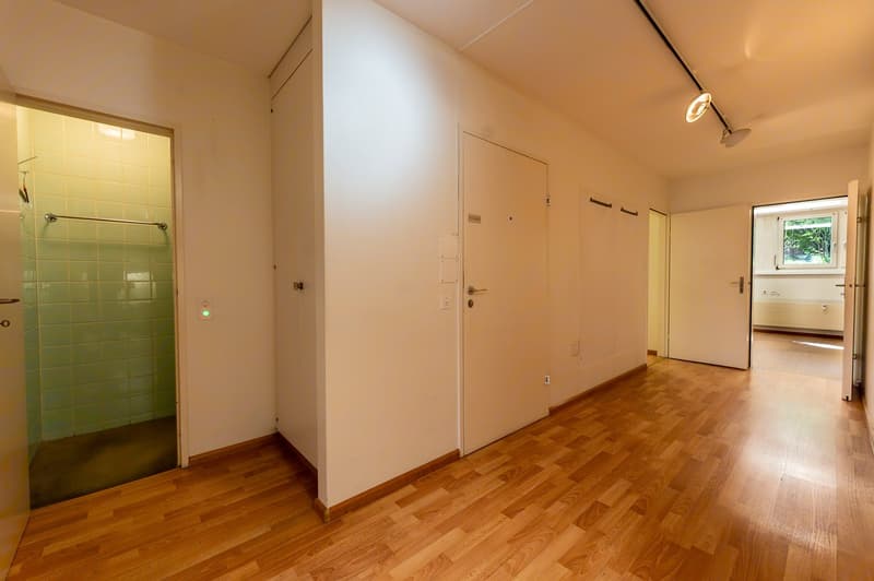 An empty room with wooden floors and white walls. There are two doors, one of which leads to a shower area. There is another open door that shows an adjacent room with a window.