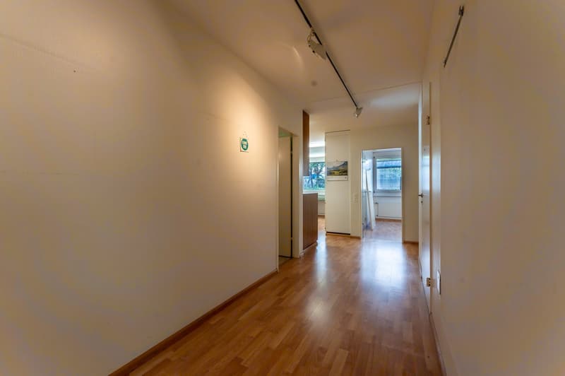 Empty hallway with wooden floor, white walls, and doors leading to other rooms.