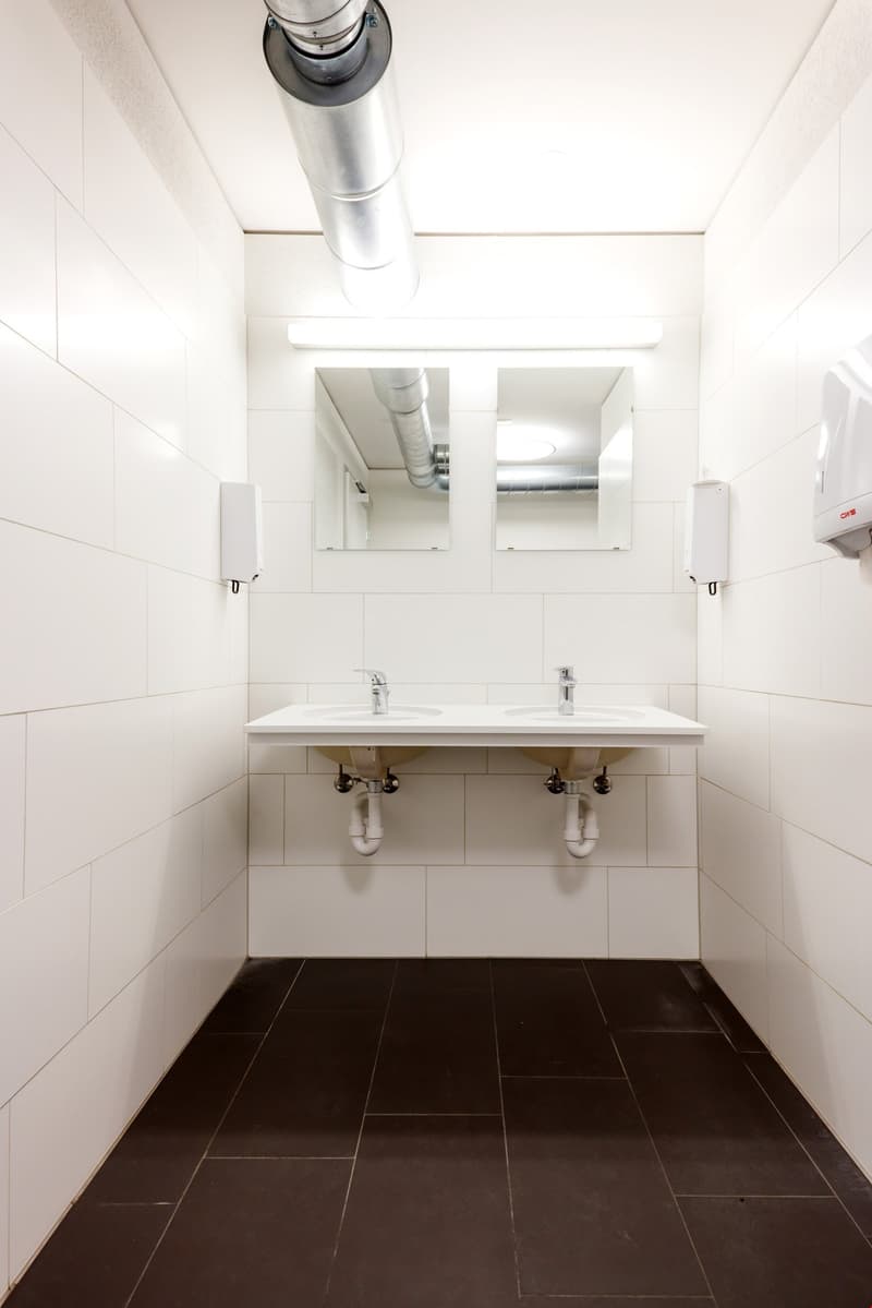 White tiled walls, double sink vanity, mirrors, dark tile flooring