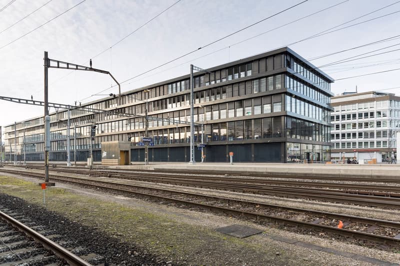 modern office building with many windows, multiple stories, located next to train tracks
