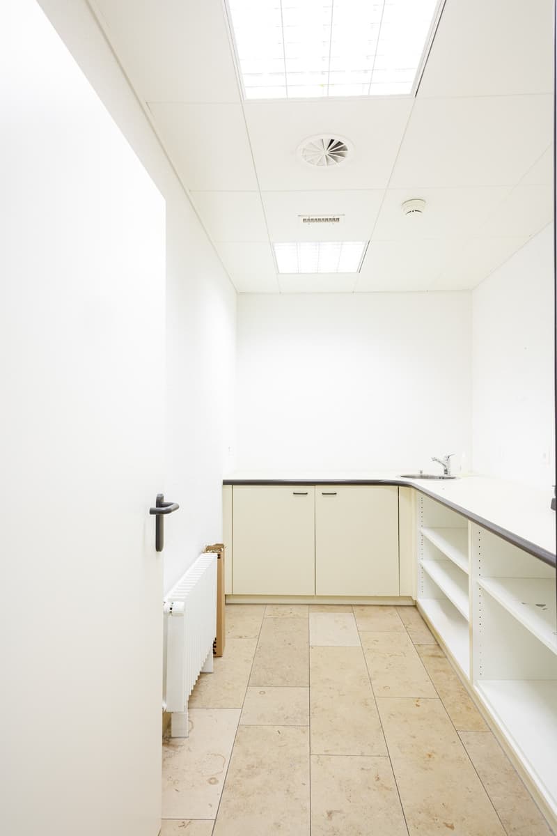 empty kitchen with white tiled floor, cabinets, sink, shelves, radiator