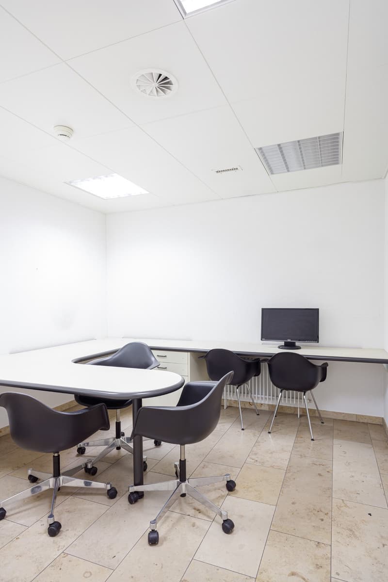 An empty office room with white walls, a desk, and black chairs.