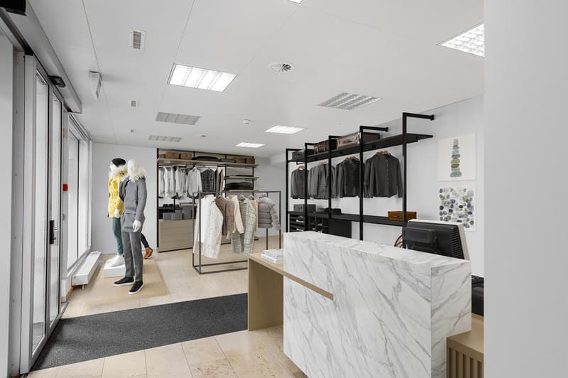 modern store with white walls, marble counter, glass doors, clothing racks, mannequins, monitor, wooden desk, black carpet