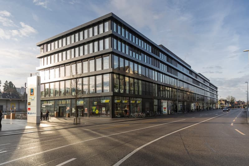 modern office building, glass facade, multiple floors, rectangular shape, located on a street with road, sidewalks, bicycles parked outside