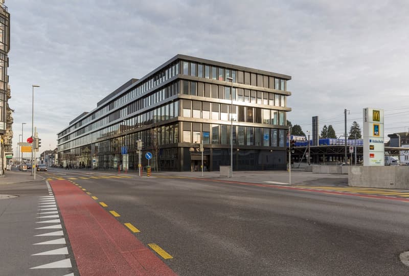 Modern office building with glass facade, multiple floors, and an entrance facing the road.