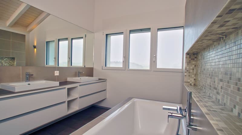 Spacious bathroom with large windows, double vanity sink, tiled walls, and a bathtub