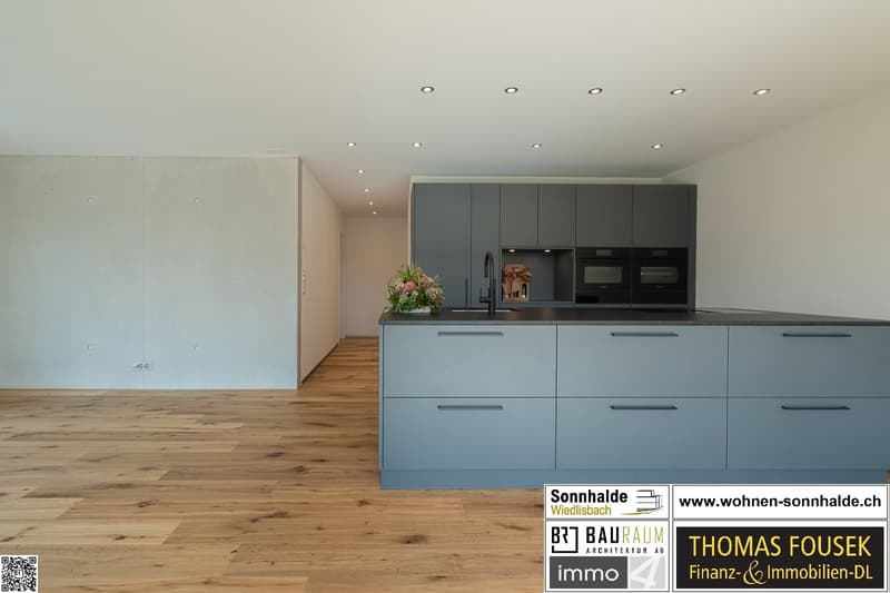 modern kitchen, wooden floor, grey cabinetry, central island, built-in ovens and microwave, granite countertops, flowers, under cabinet lighting, dishwasher, washing machine