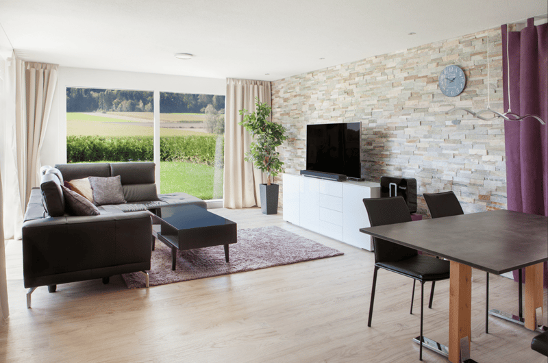 large windows, modern furnishings, grey sofa, flat screen TV, coffee table, rug, wooden dining table