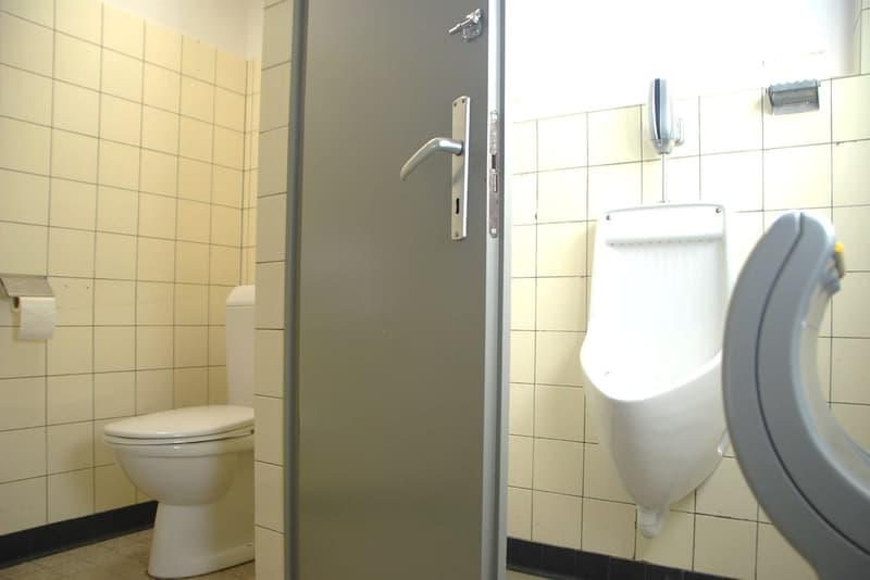 Standard white toilet, a wall-mounted urinal, a toilet paper holder, and tiled walls.