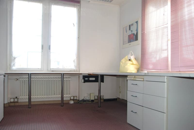 empty office room with windows, radiator, desk, drawers, yellow bag