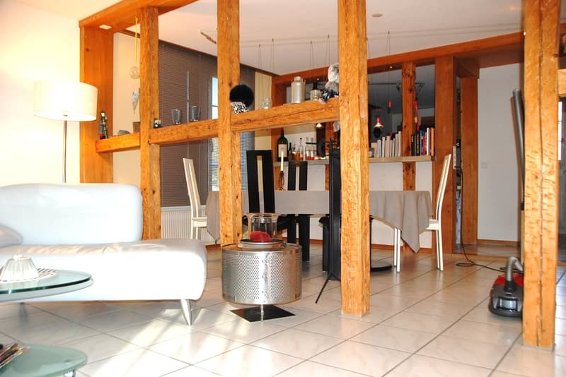 modern living room with white couch, wooden pillars, tiled floor, coffee table, lamp, table with chairs, shelves with items, and a table with a tablecloth