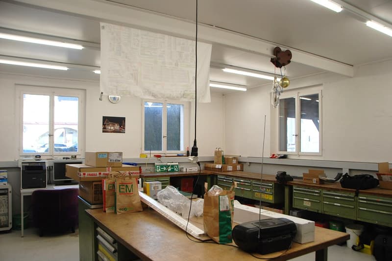 Empty room with multiple tables, chairs, and boxes on the ground.